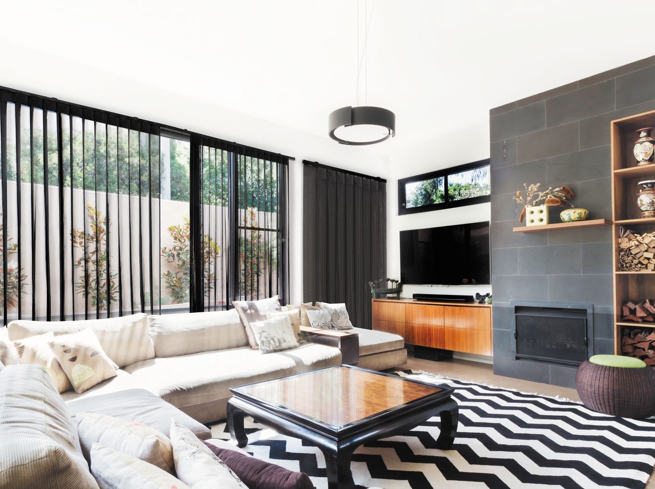 A modern living room with a gray sectional sofa, a chevron rug, and a slate-tiled fireplace wall with built-in shelving.