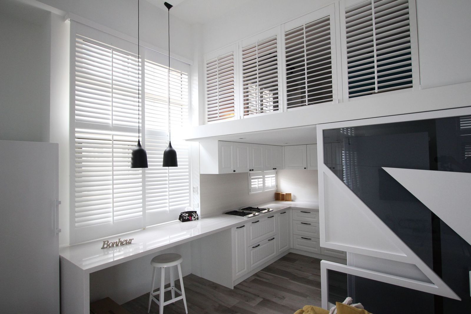 Modern white kitchen with a breakfast bar, two pendant lights, and louvered shutters above the cabinets.