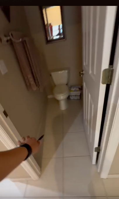 A person's arm reaches into a small bathroom with a toilet and a towel rack on the wall.