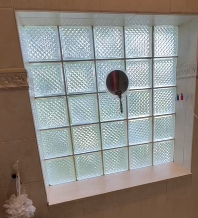 A glass block window with a small, circular suction-cup mirror attached to the center pane, set in a tiled wall.