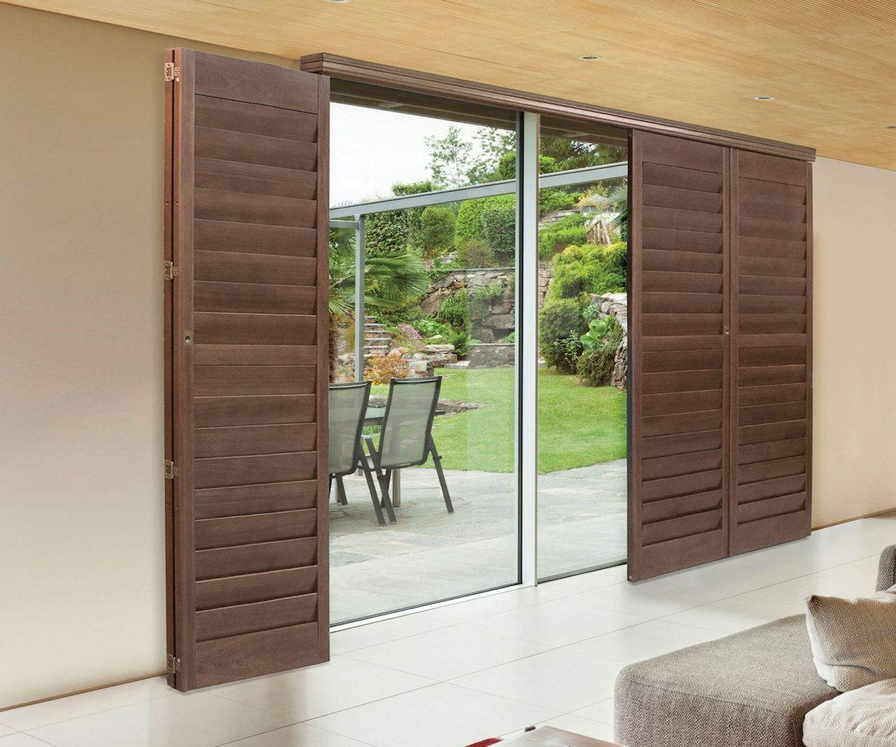 Brown louvered shutters partially covering a sliding glass door that leads to a patio and garden.