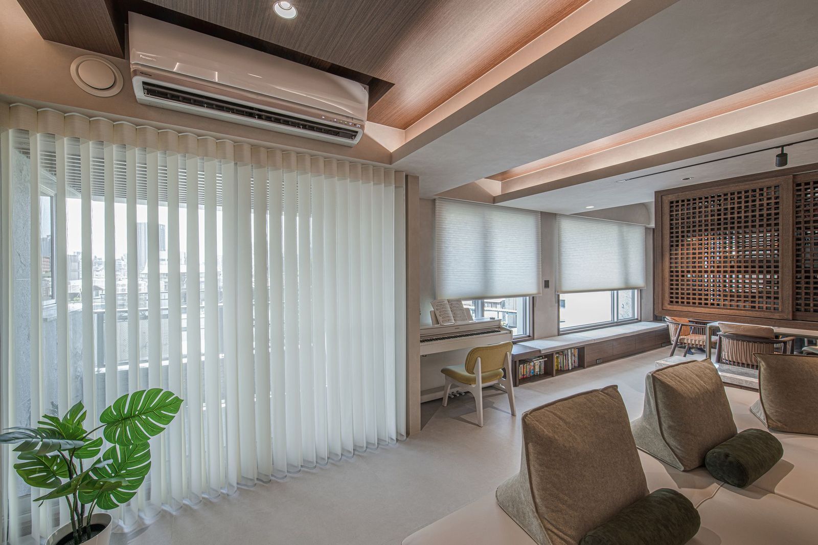 A bright, modern interior room with tall sheer curtains, neutral furniture, a minimalist desk, and indoor greenery.