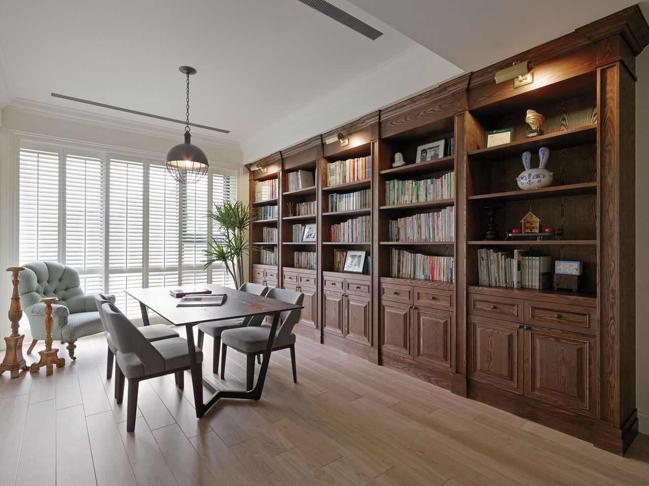 A dining area with a wood table, four gray chairs, and a large, dark wood built-in bookcase against a paneled wall.