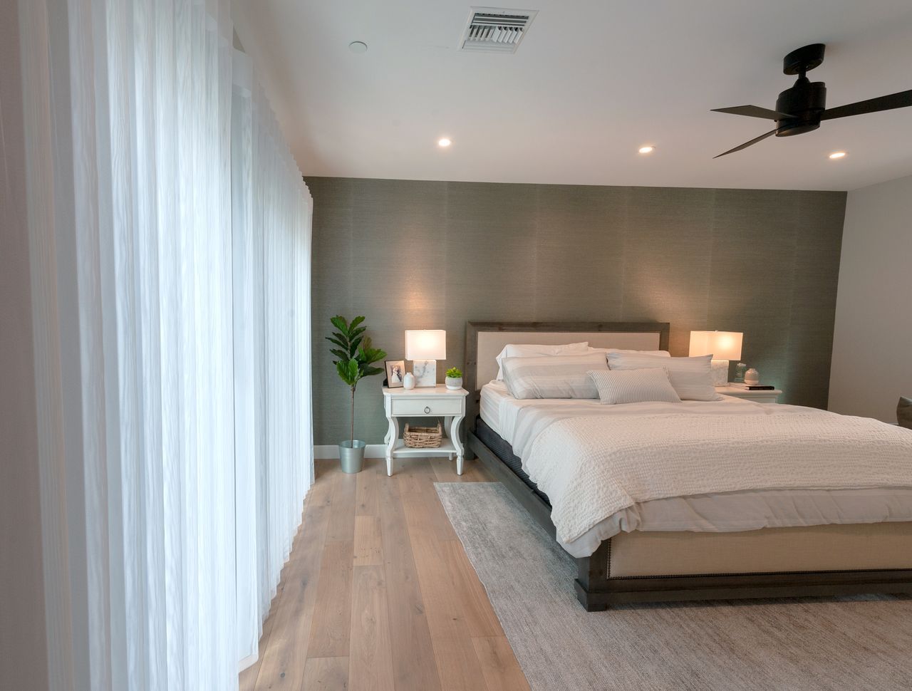 A bedroom with a textured olive-green accent wall, light wood floors, and floor-length curtains.