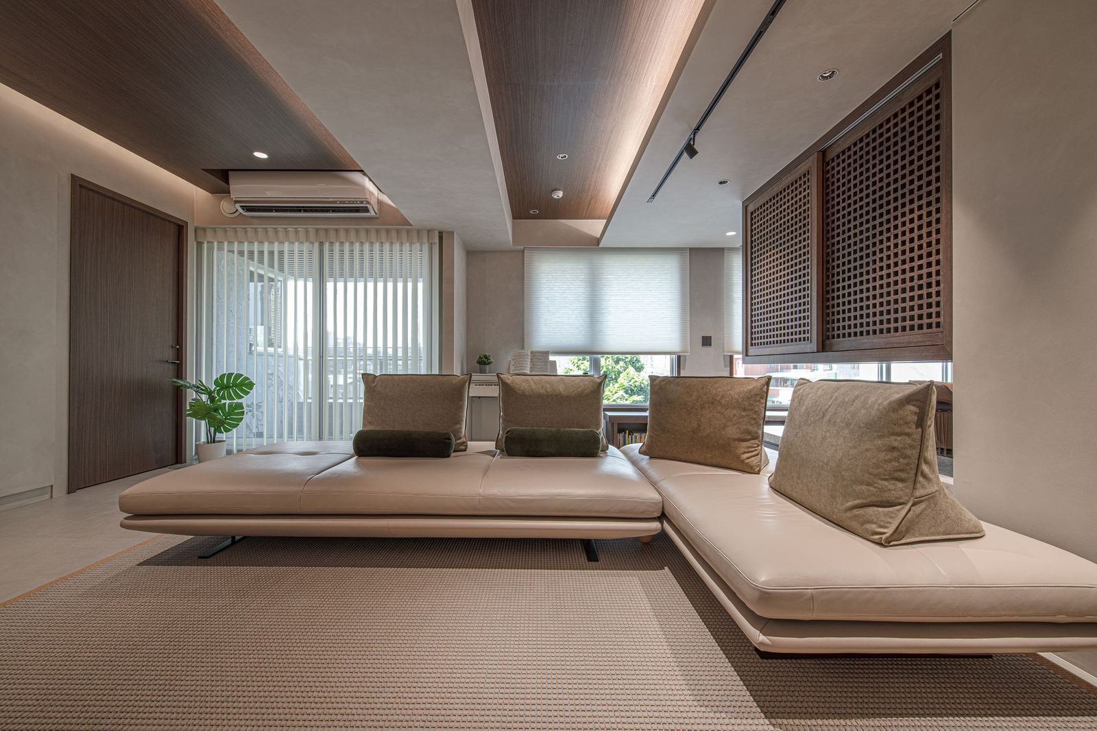 Modern living room with a neutral-toned sectional sofa, wood-paneled ceiling, and window blinds.