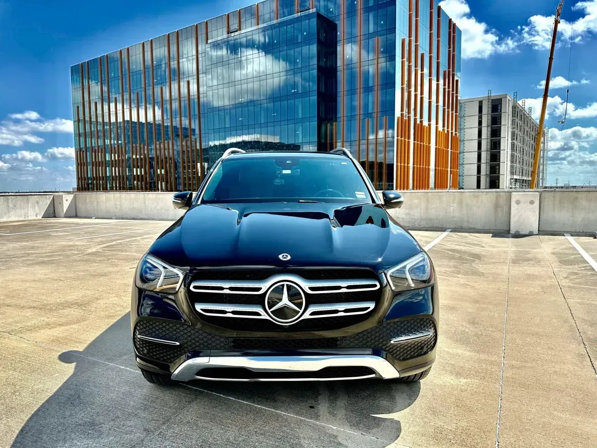 Black Mercedes SUV parked in front of a modern glass building with a bright sky.