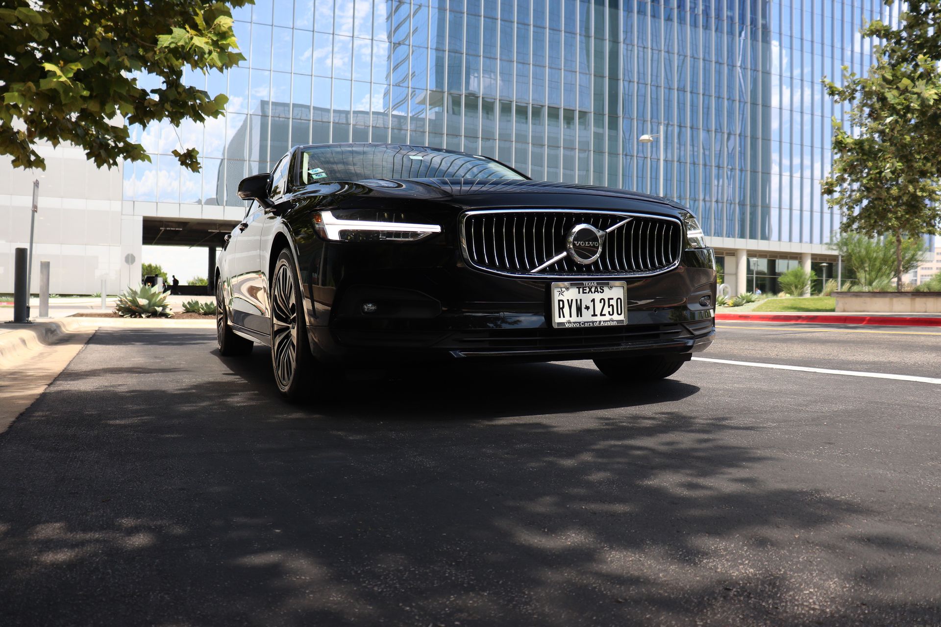 Black Volvo sedan parked on asphalt in front of a modern glass building; Texas license plate.