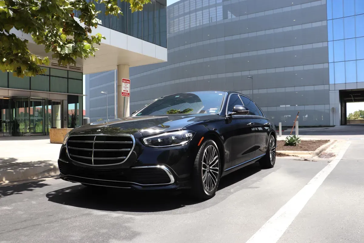 Black Mercedes sedan parked in front of a modern building with glass windows.