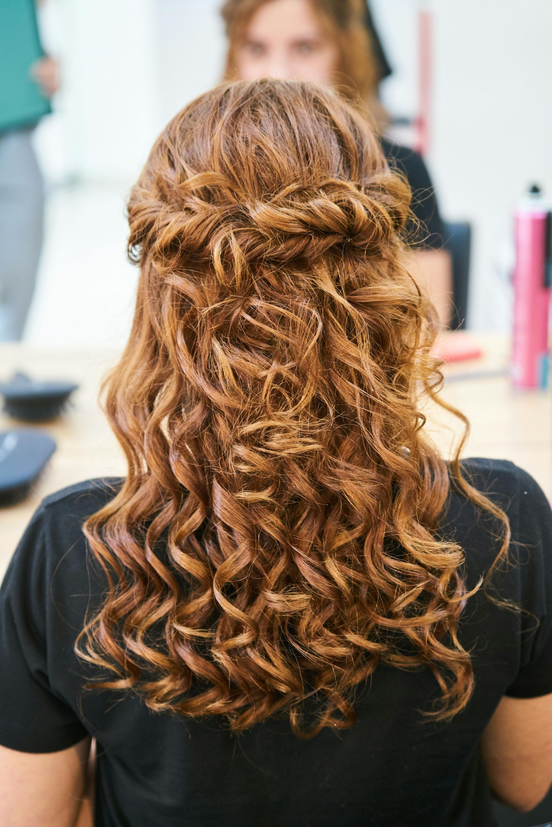A woman with curly hair is wearing a black shirt and has her hair in a half up half down hairstyle.
