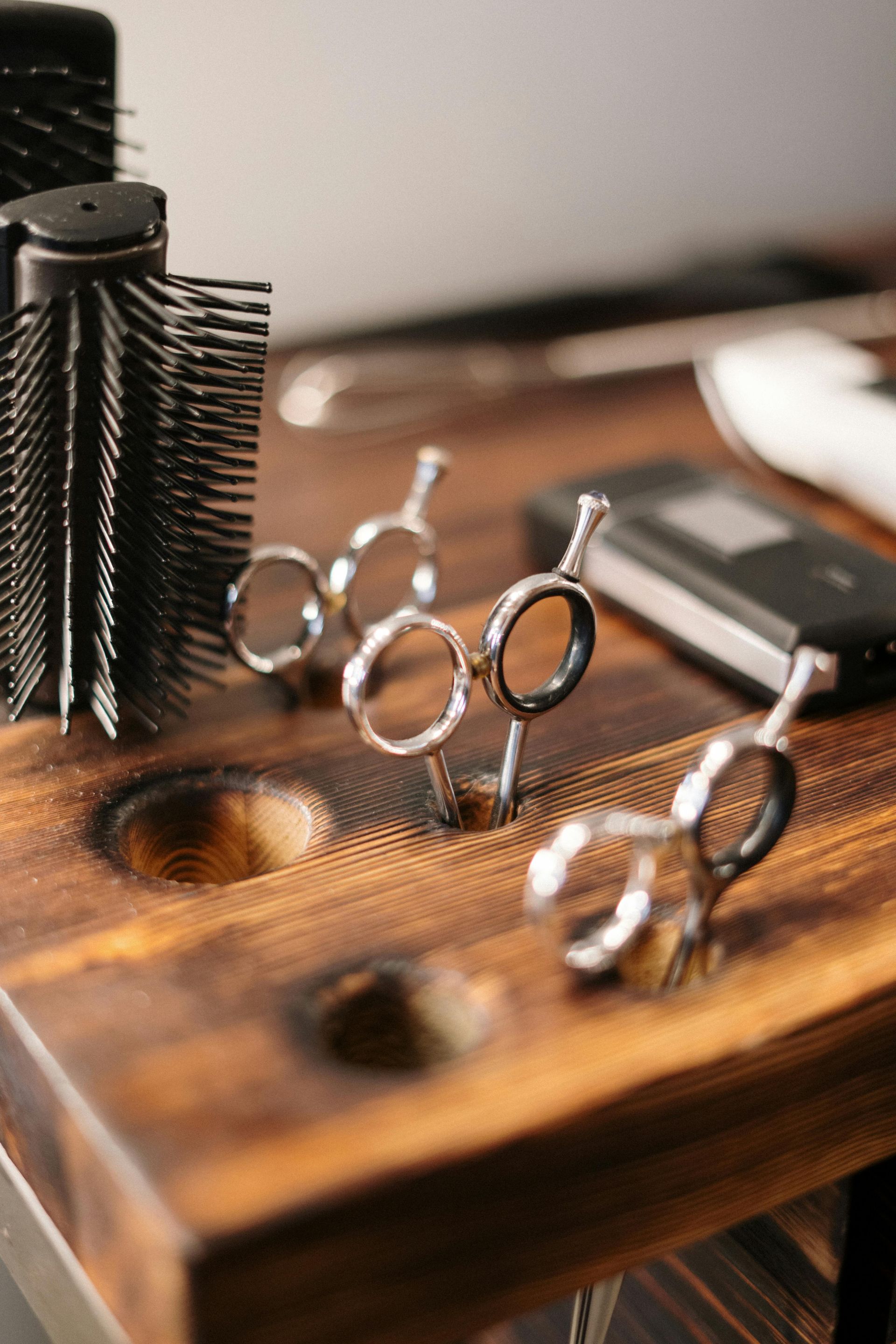 A pair of scissors and a brush are sitting on a wooden table.
