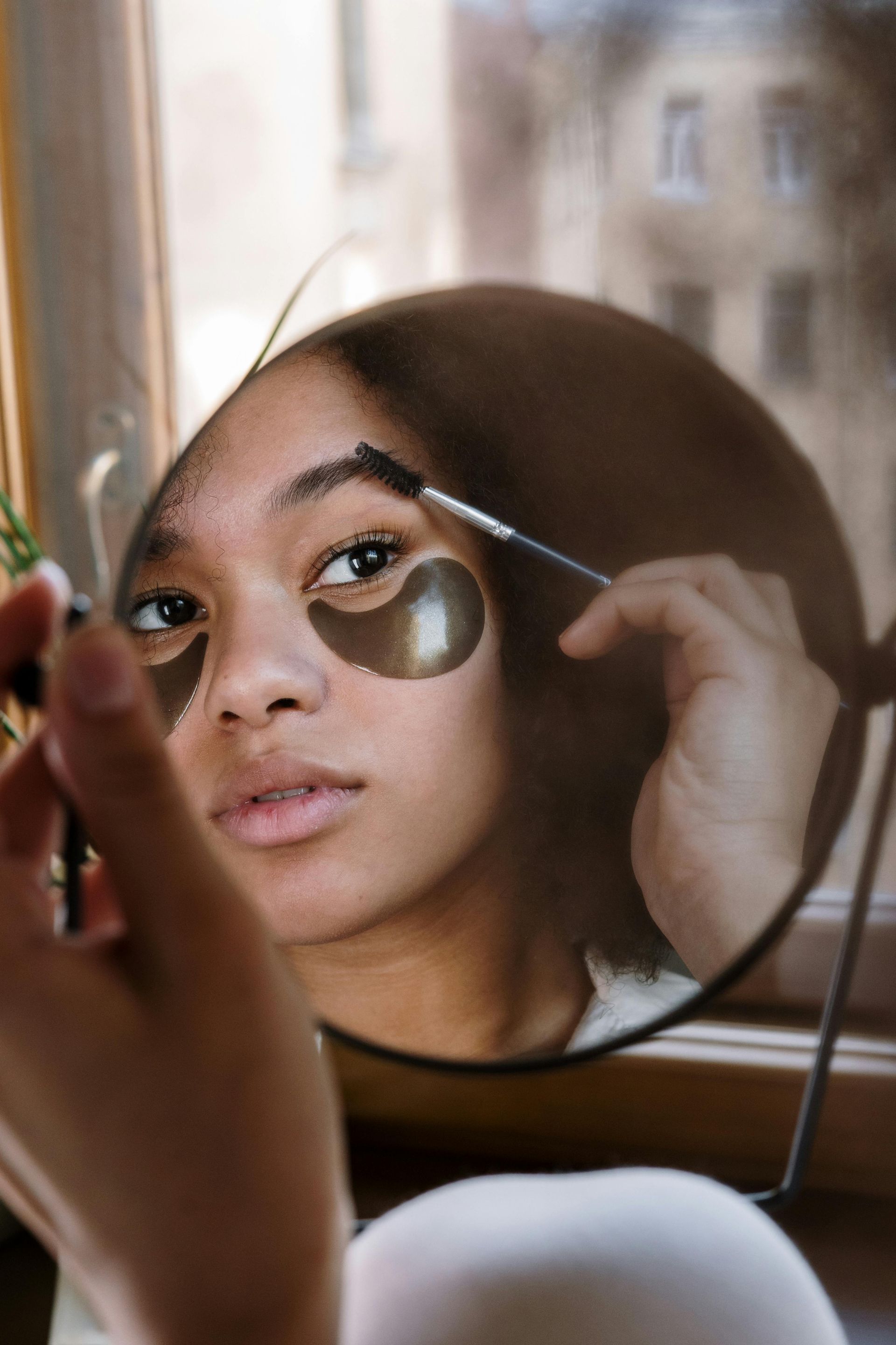 A woman is applying makeup to her eyebrows in front of a mirror.