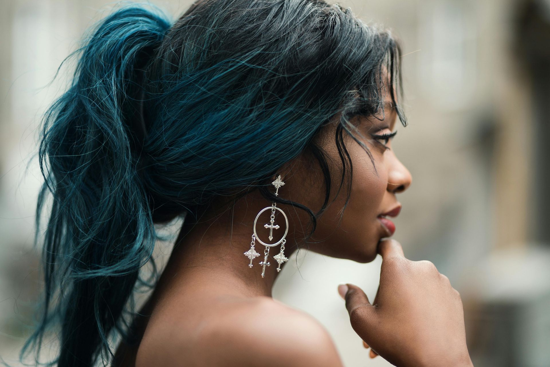 A woman with blue hair is wearing earrings and a ponytail.