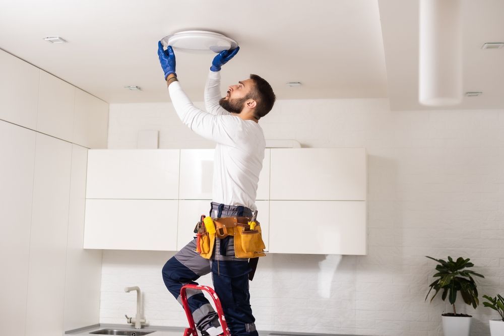 A man is installing a light fixture on the ceiling in a kitchen.