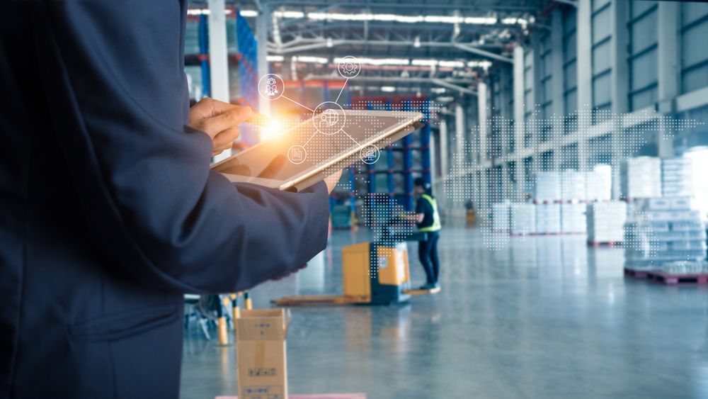 A man is holding a tablet in a warehouse.