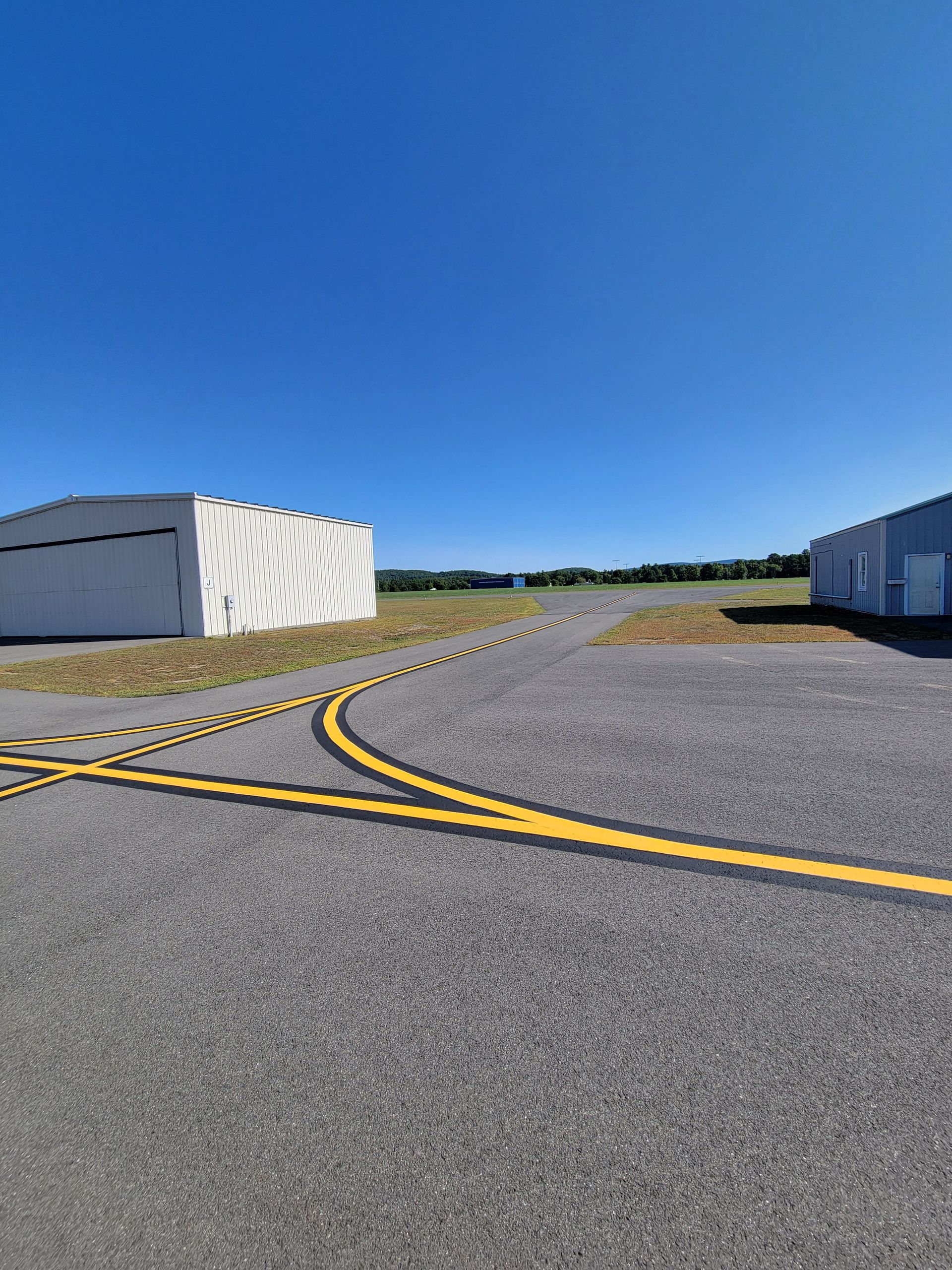 Asphalt runway with yellow markings, buildings on each side, under a clear blue sky.