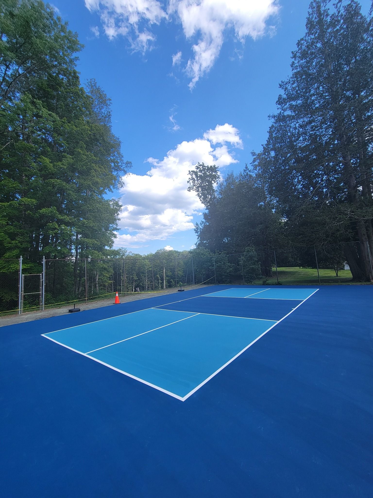 Asphalt parking area with white painted lines and dotted spots, next to a building and trees.