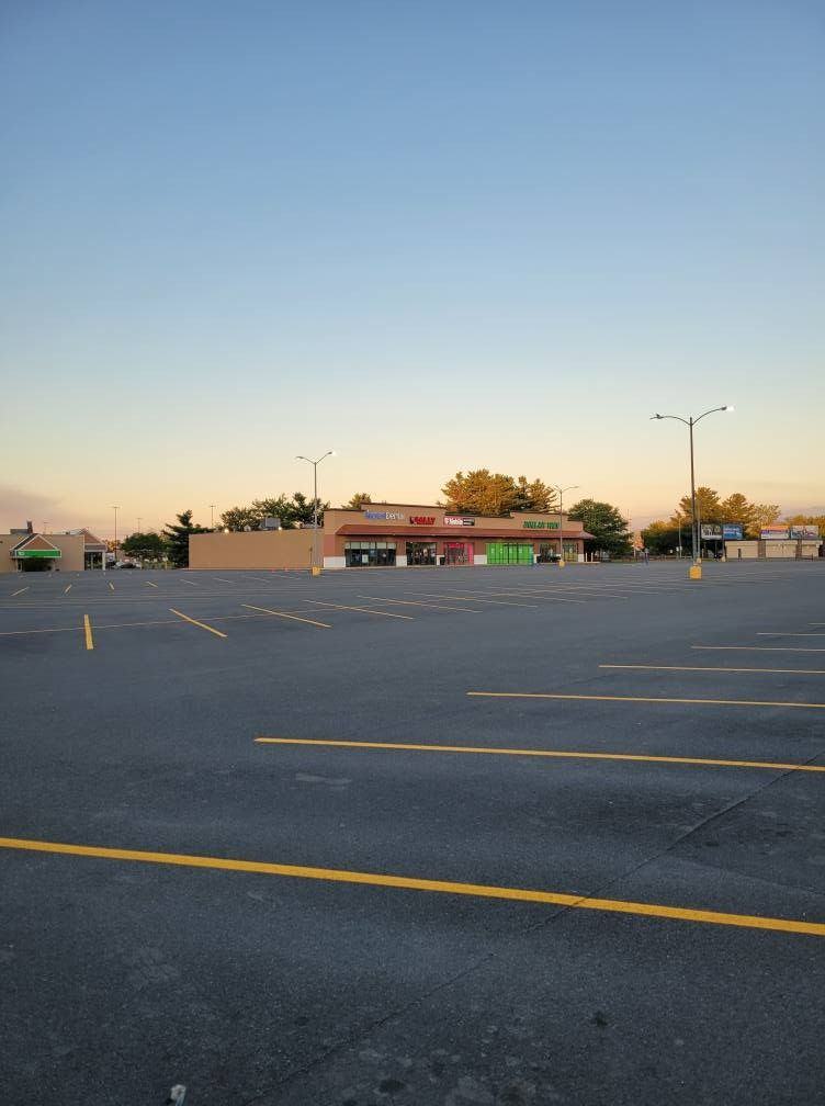 Empty asphalt parking lot with a single-story building in the distance under a blue sky.