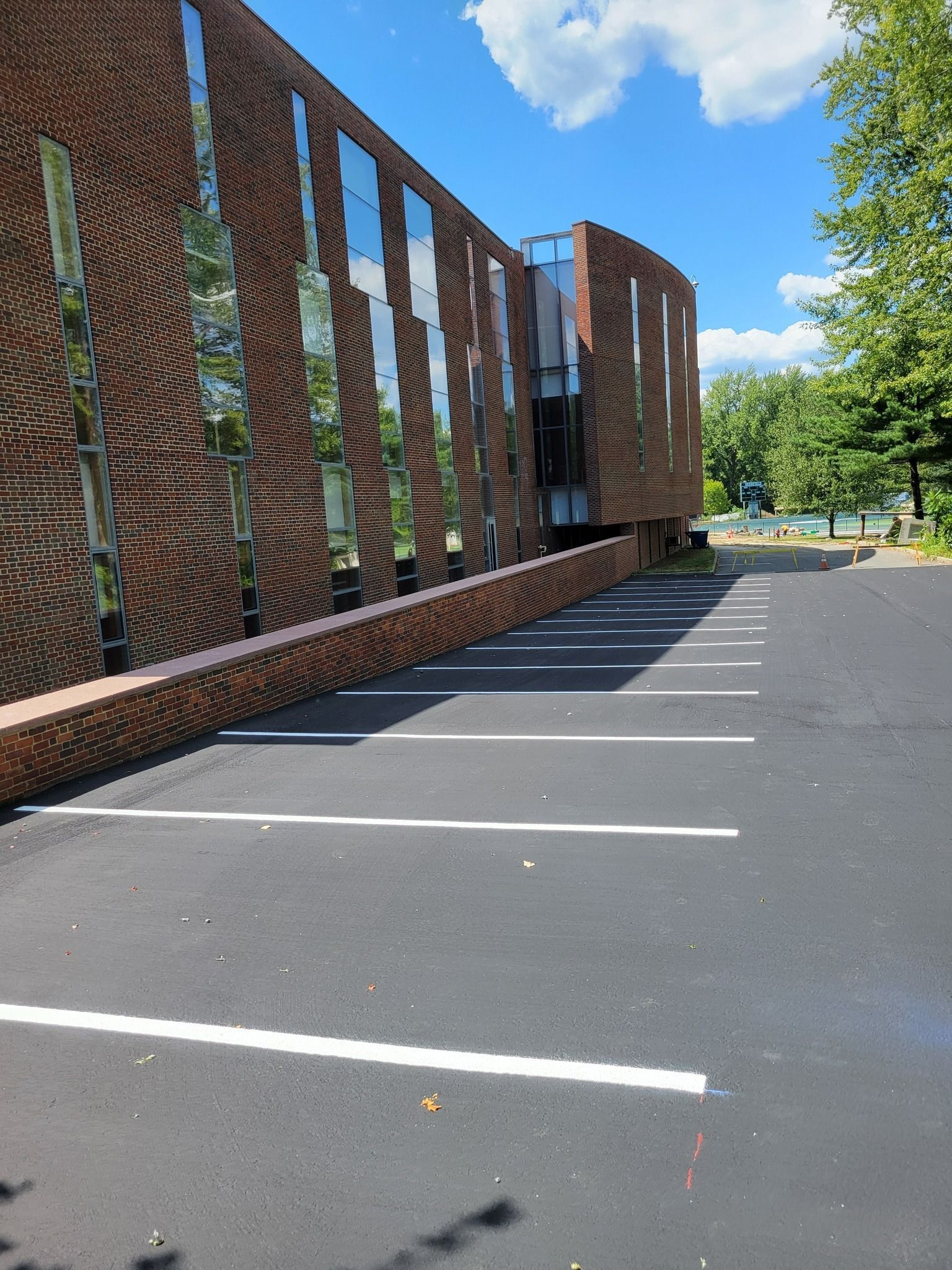 Brick building with reflective windows and a newly paved parking lot on a sunny day.