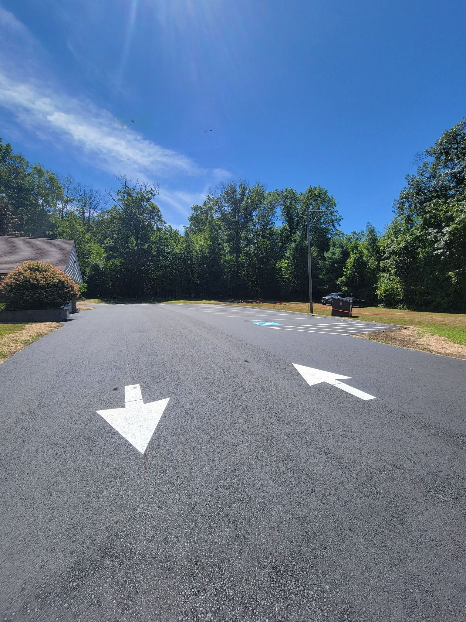 Asphalt driveway with white directional arrows and children's hopscotch game. Trees in background, bright blue sky.