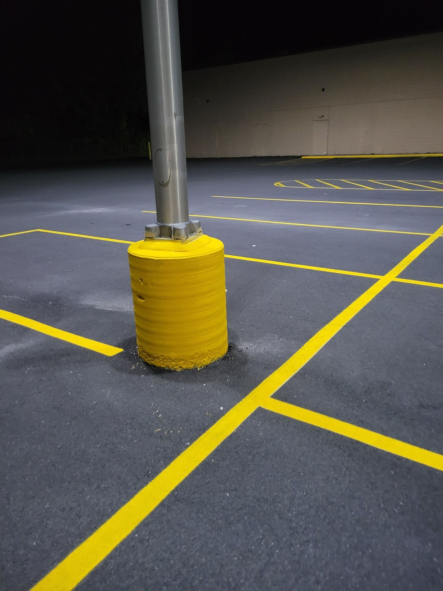 Yellow parking lines on dark asphalt around a gray pole base, under a street light.