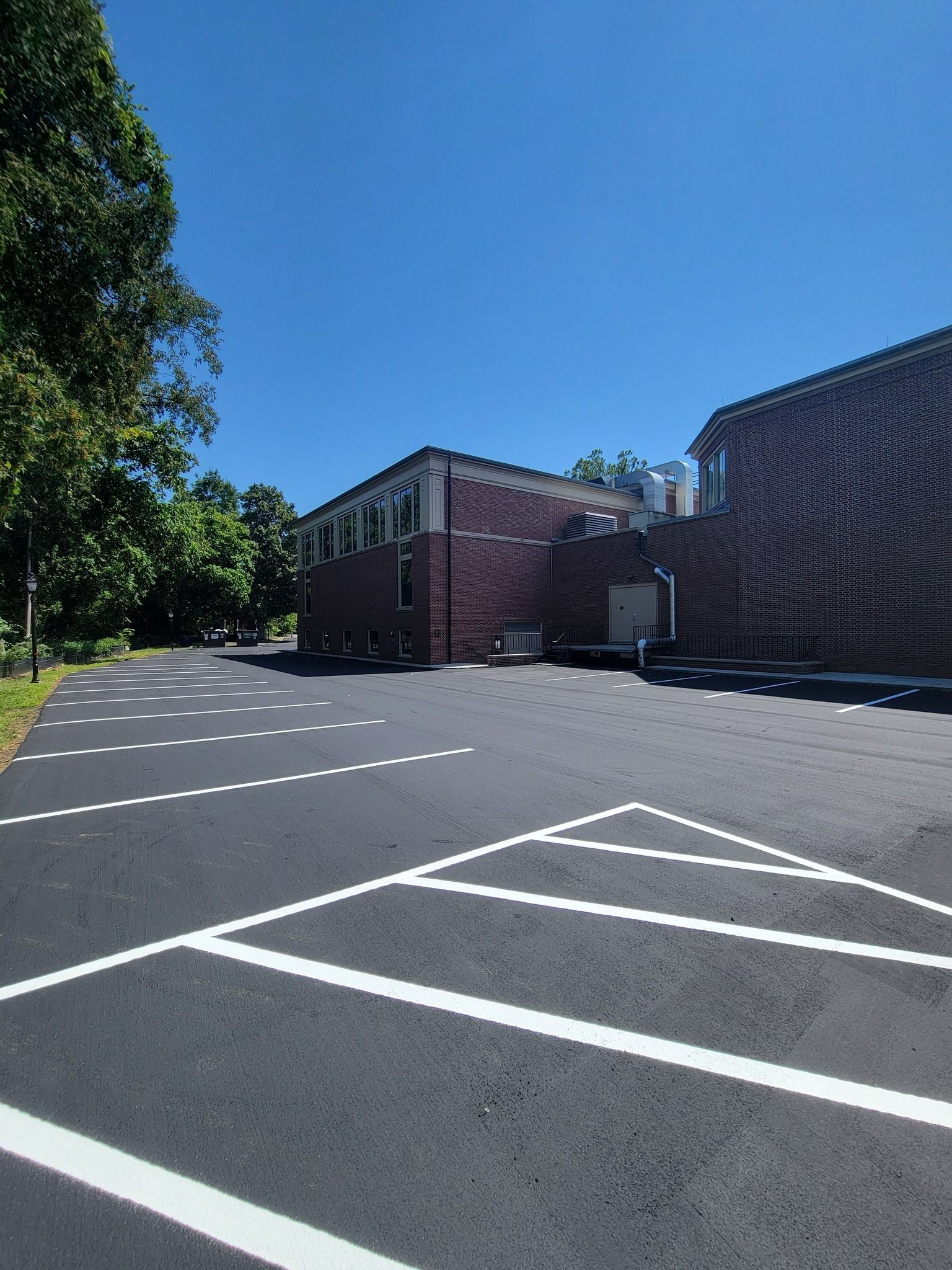 Asphalt parking lot with white painted parking space markers in front of a brick building under a clear blue sky.
