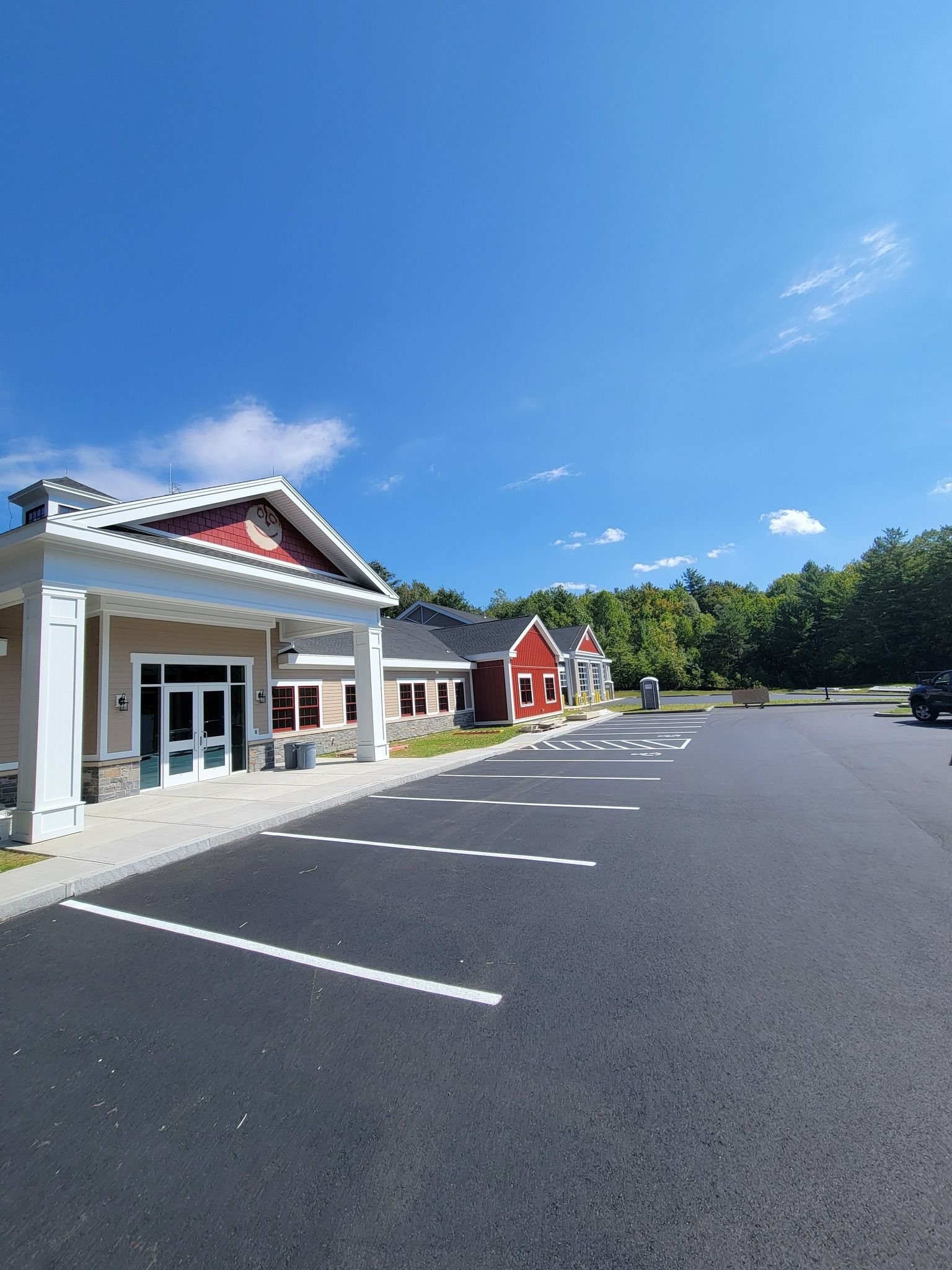 New asphalt parking lot in front of several buildings. Bright blue sky with a few clouds. Buildings have red and tan siding.