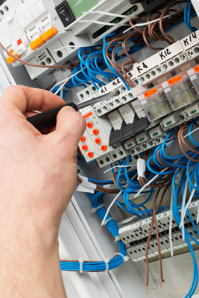 A person is working on an electrical box with a screwdriver.