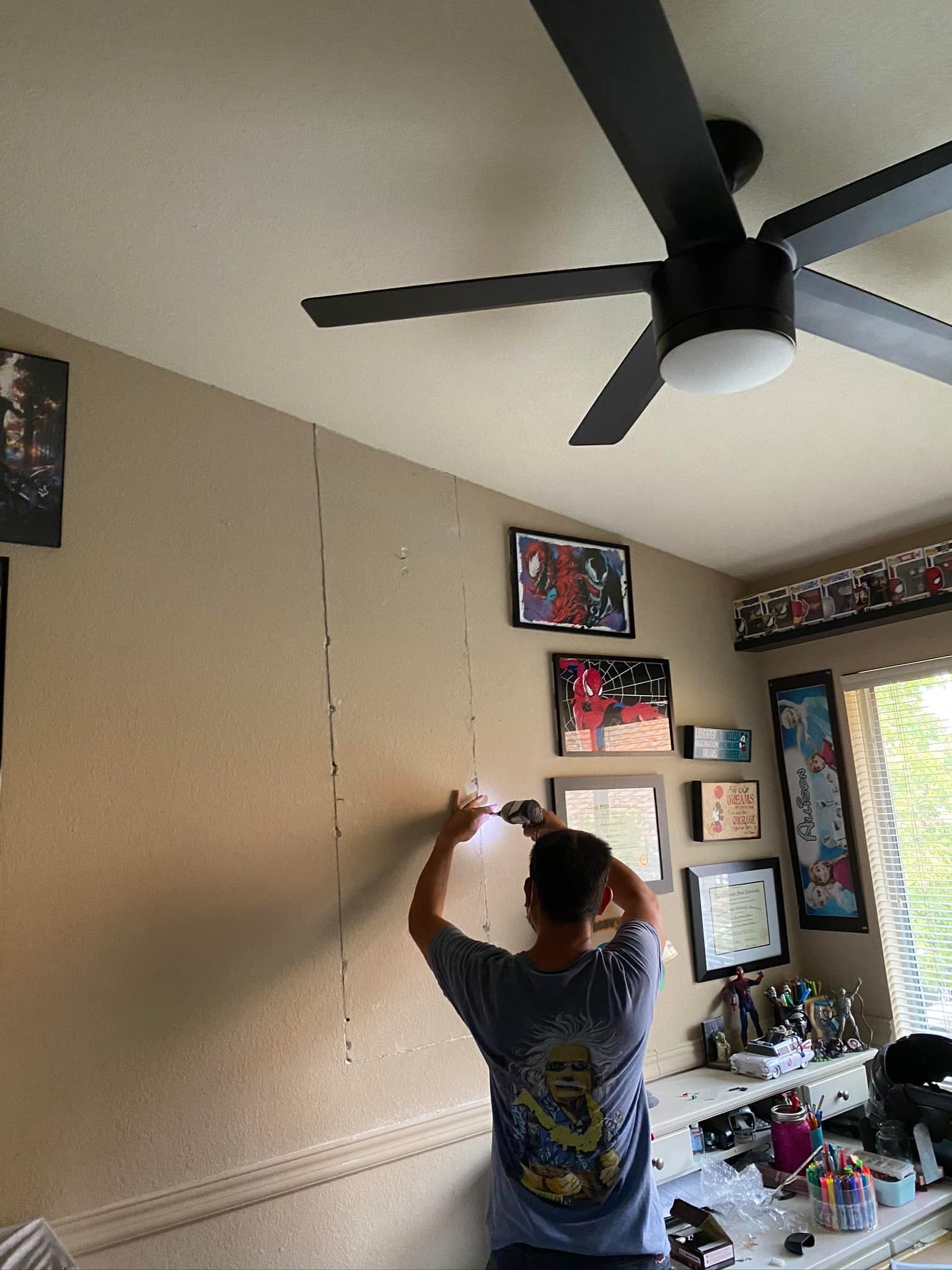 A woman is working on a wall in a room with a ceiling fan.