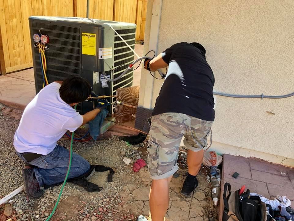 Two men are working on an air conditioner outside of a house.