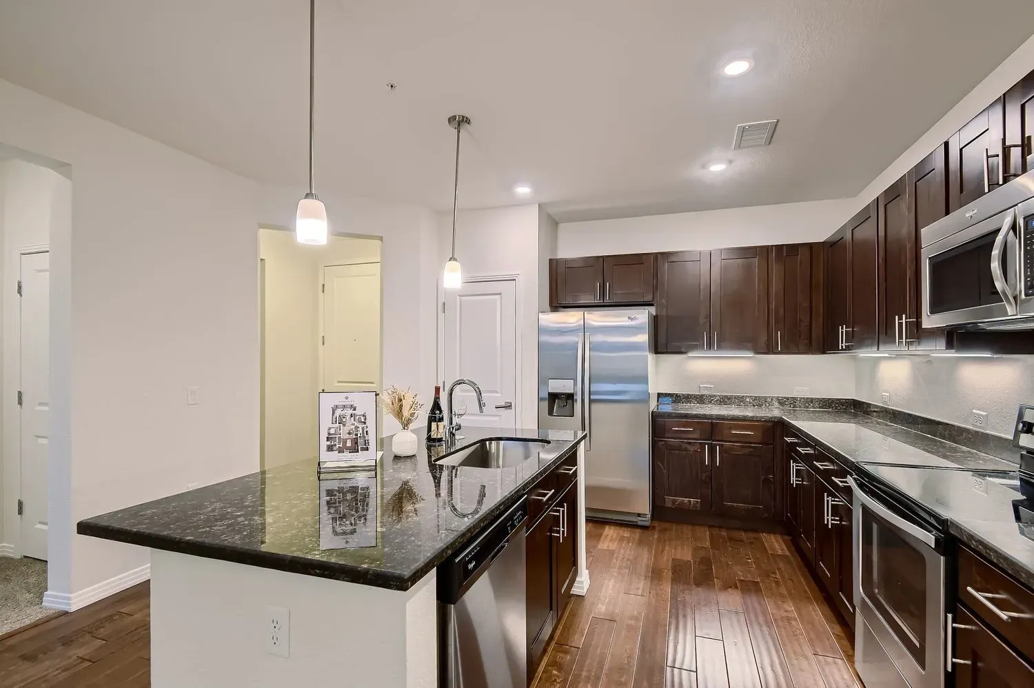 Modern kitchen with dark wood cabinets, granite island, stainless appliances, and hardwood floors.