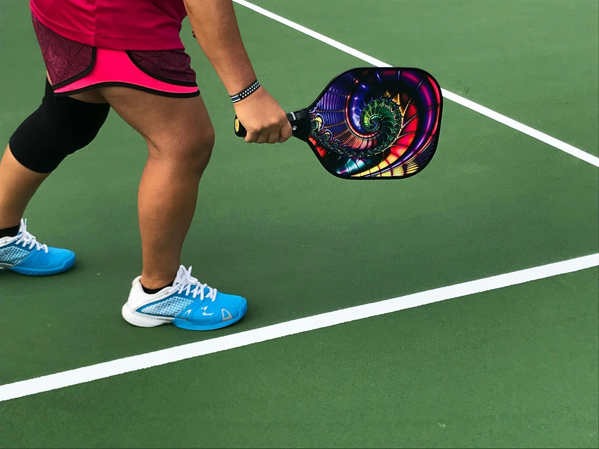 Person in pink shorts holding a colorful pickleball paddle on a green court.