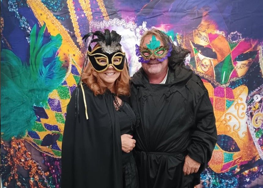 Two people in colorful feathered masquerade masks posing before a vibrant mural.