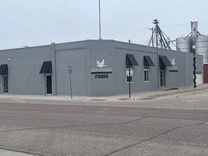 Gray industrial building with black awnings and a logo sign on a street corner