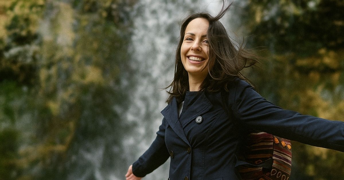 Smiling young woman with arms outstretched in front of a waterfall