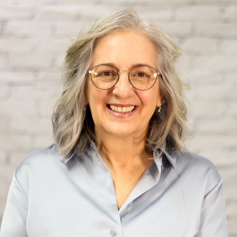 A woman wearing glasses and a blue shirt is smiling for the camera.