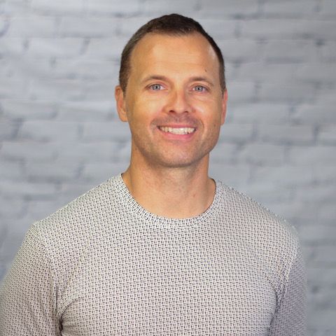 A man in a sweater is smiling in front of a brick wall.
