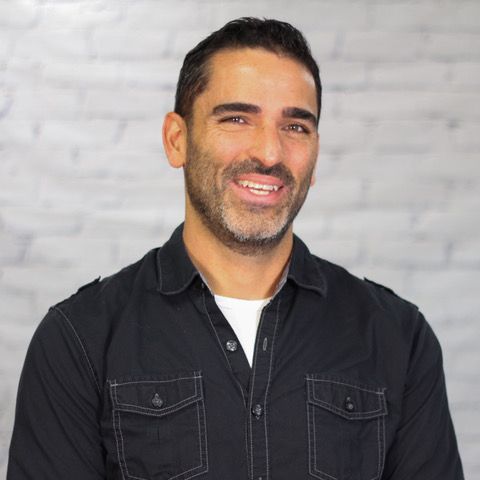 A man with a beard is wearing a black shirt and smiling.