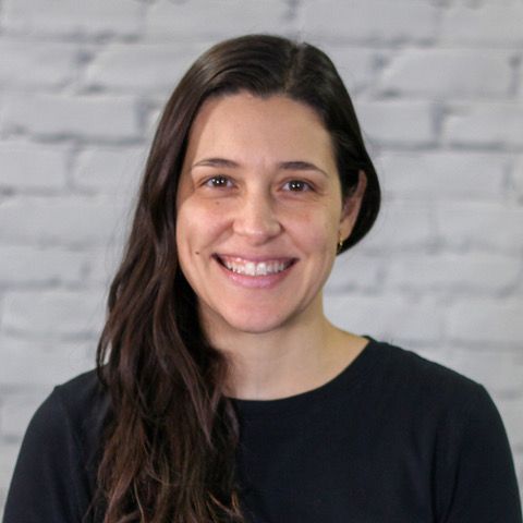 A woman is smiling for the camera in front of a white brick wall.
