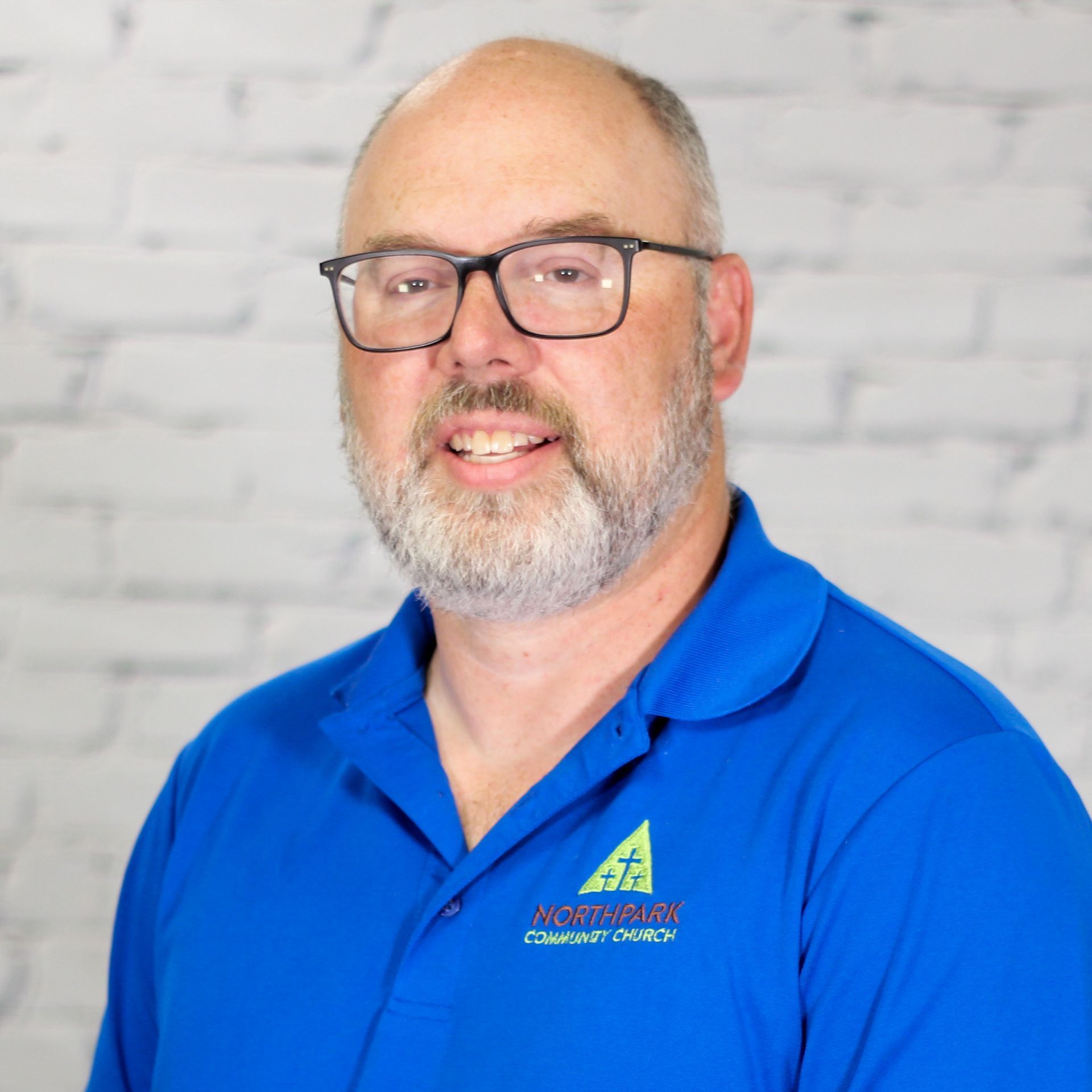 A man with glasses and a beard is wearing a blue shirt that says northpark community church