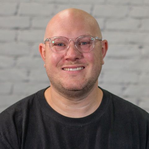 Josh Black wearing  a blue jays hat and glasses is smiling for the camera.