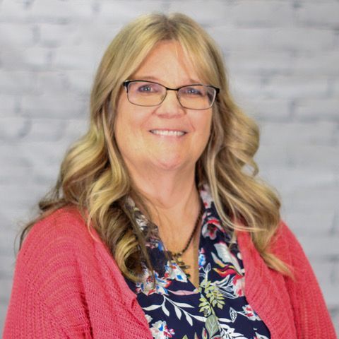 A woman wearing glasses and a pink sweater is smiling for the camera.