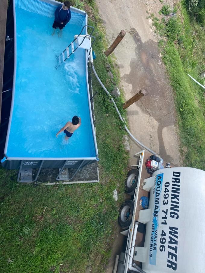 A Man Is Swimming In A Pool Next To A Drinking Water Truck — Aquaman Watàr Deliveries In Bald Knob, QLD