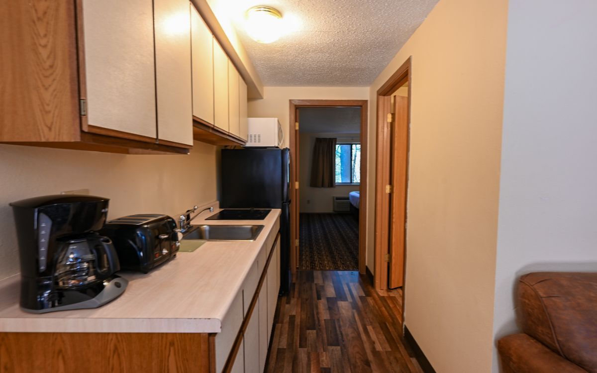 Kitchen with light-colored countertop, cabinets, and appliances; a doorway leads to a bedroom.