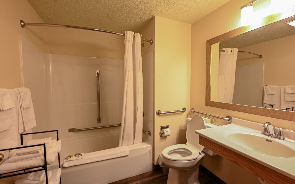 Bathroom with tub/shower, toilet, and sink. Beige walls, white shower curtain, and a towel rack with folded towels.