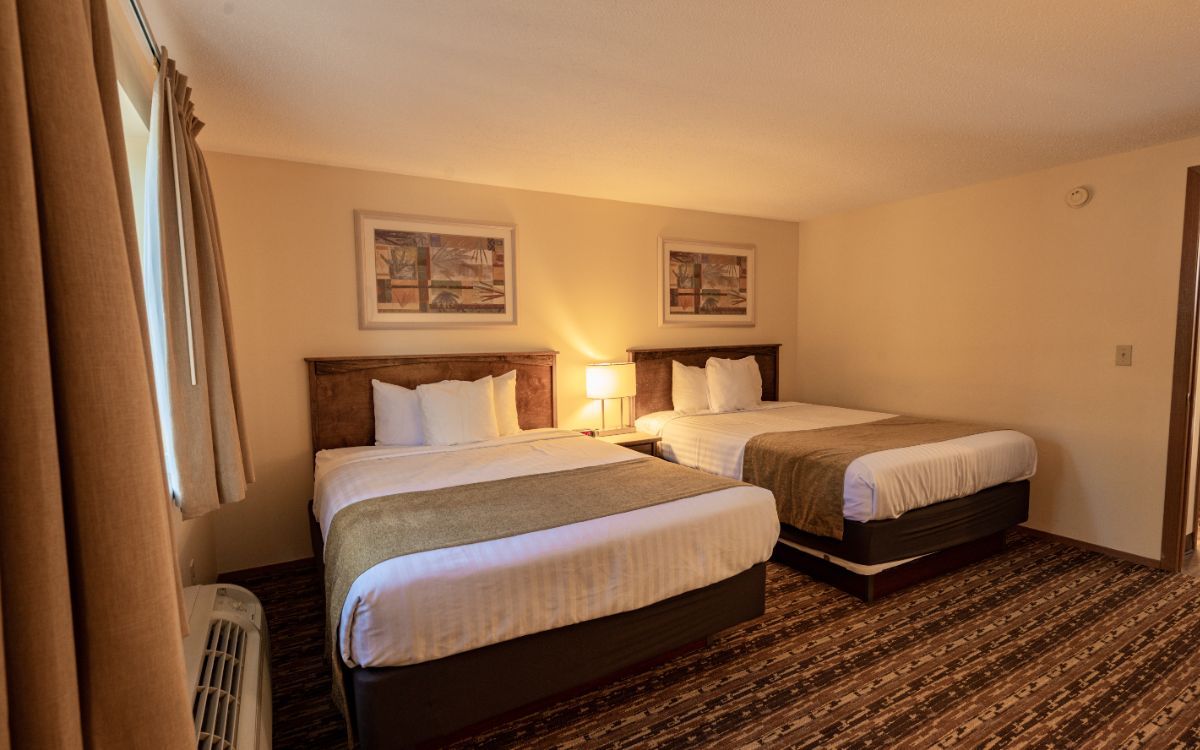 Two beds in a hotel room with tan walls, brown bedspreads, and a window.