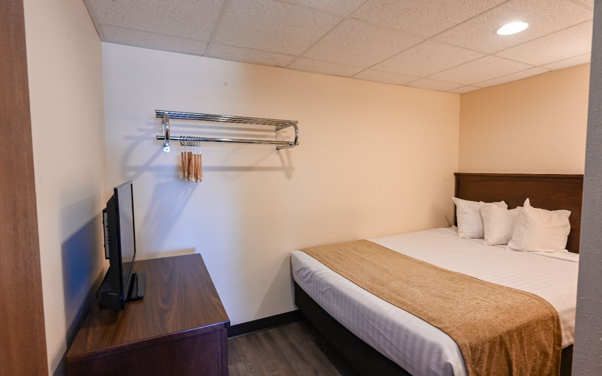 A hotel room with a bed, TV, dresser, and wall-mounted clothes rack.