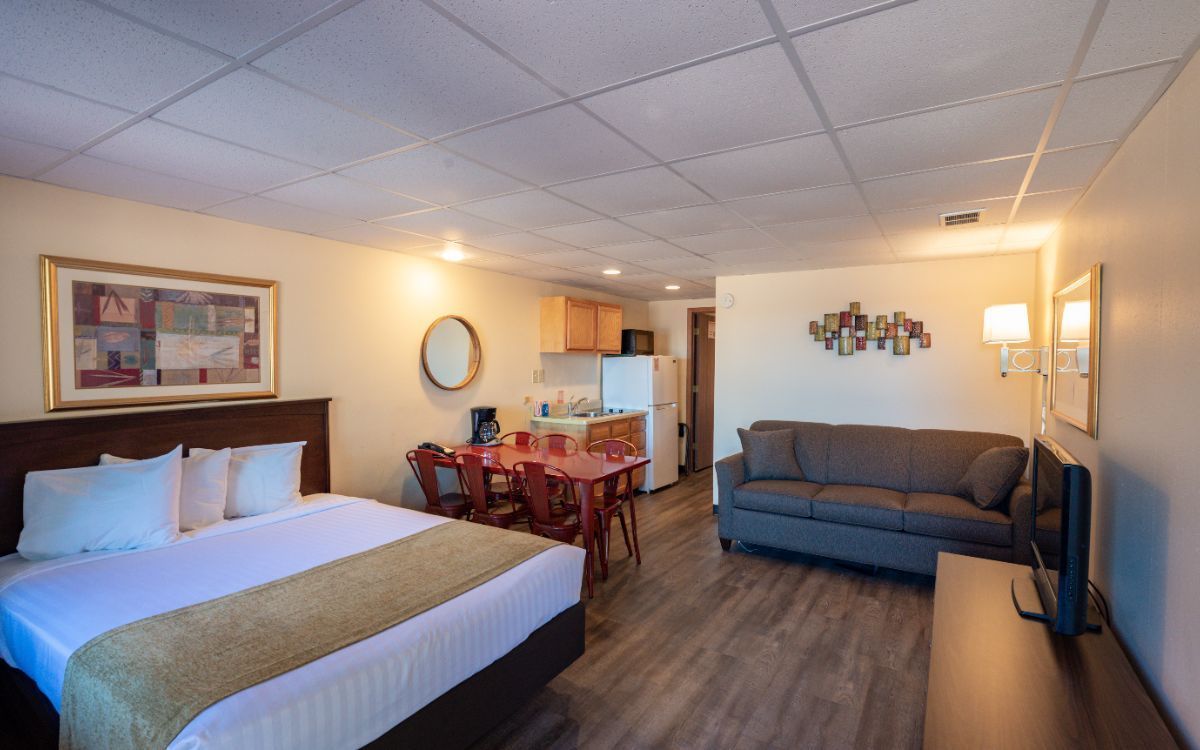 Studio apartment with a bed, small kitchen, dining area, and sofa. Wooden floors, beige walls.