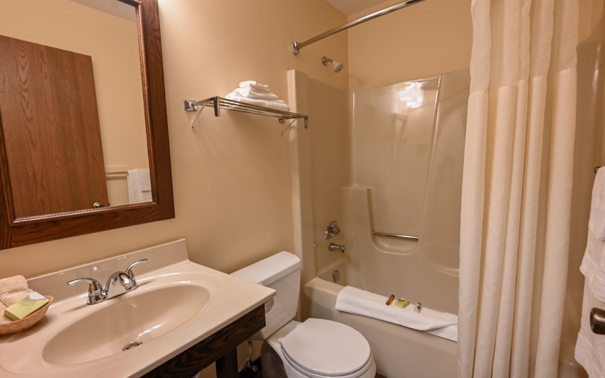 Bathroom with a sink, toilet, tub/shower, towels, and mirror. Beige walls and white fixtures.