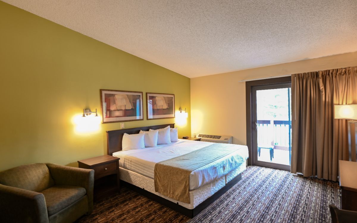 Bedroom with a bed, chair, and sliding door to a balcony. Green walls, brown carpet, and two framed pictures.
