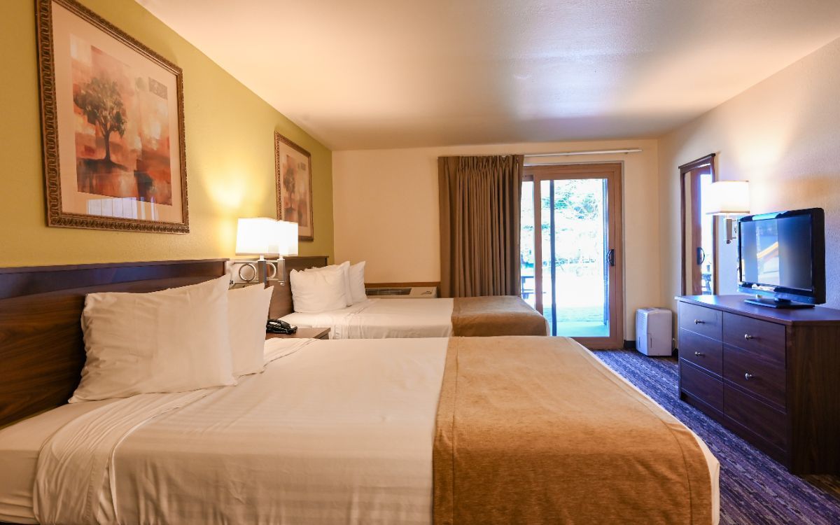 Hotel room with two beds, TV, dresser, and sliding door to the outside.